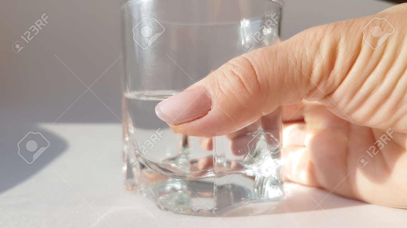 Close-up of female hand holding transparent glass with cold water on white background - 168250810 Close-up of female hand holding transparent glass with cold water on white background - 168250810