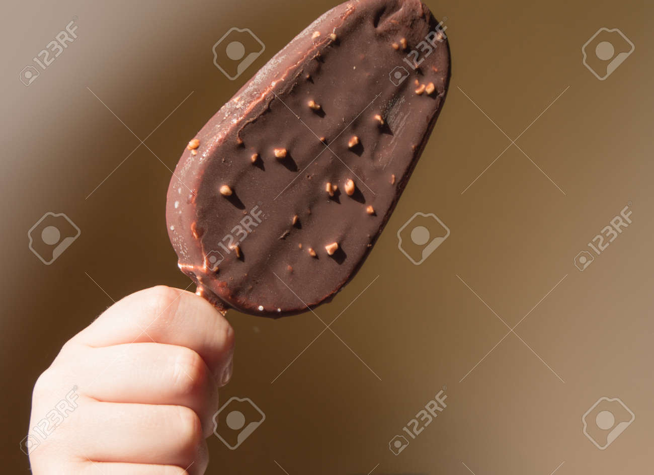 Close-up of a child holding a chocolate ice cream on a stick, on a yellow summer background. - 168986530 Close-up of a child holding a chocolate ice cream on a stick, on a yellow summer background. - 168986530