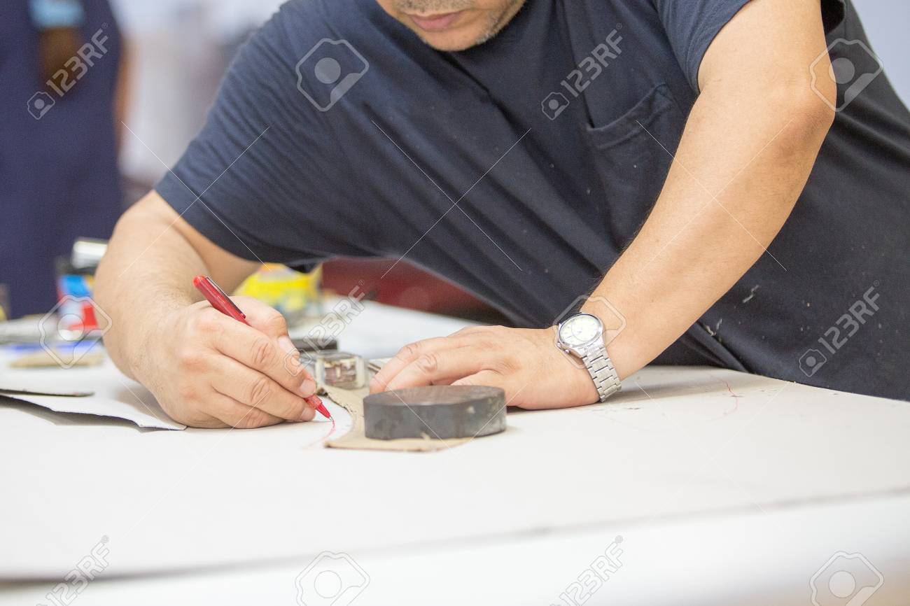 Close up of a male worker working with the pattern of the leather in the work table to upholstering the interior car components in a leather upholstery factory - 106481845 Close up of a male worker working with the pattern of the leather in the work table to upholstering the interior car components in a leather upholstery factory - 106481845