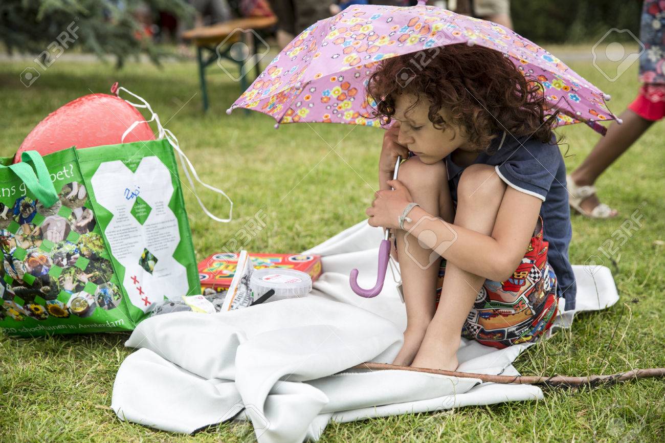 Amsterdam, Países Bajos - 5 De Julio De 2015: Niño Se Refugia De La Lluvia Debajo De Un Paraguas Pequeño Durante Roots Open Air, Un Festival Cultural Celebrado En El