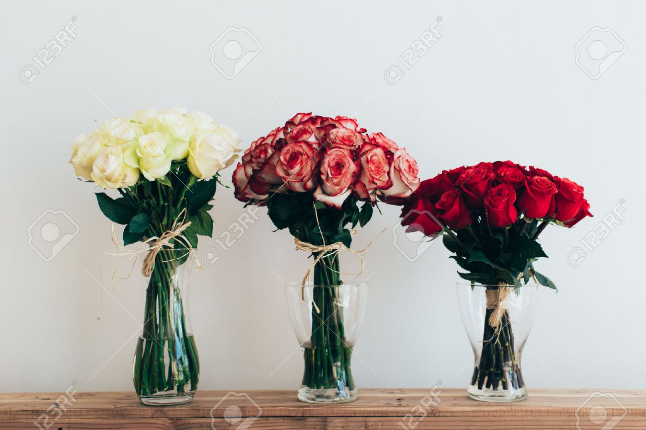 Bouquets Of Roses In Three Glass Vases Next To A Watering Can
