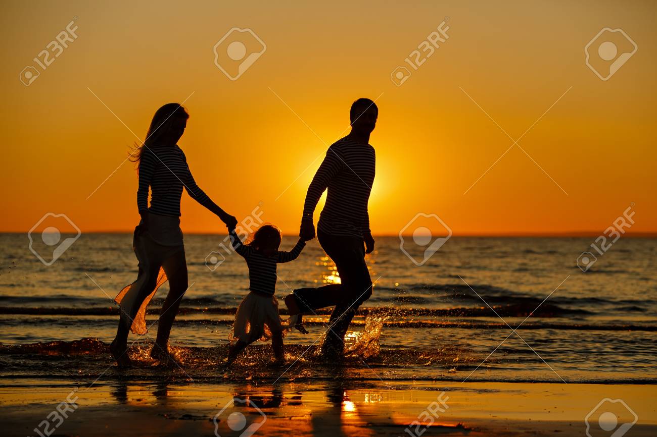 Mama Papa Y Bebe Nina En Una Falda A Rayas Y Una Chaqueta Corriendo Por El Agua Haciendo Un Chapoteo Al Atardecer En Verano Fotos Retratos Imagenes Y Fotografia De Archivo Libres