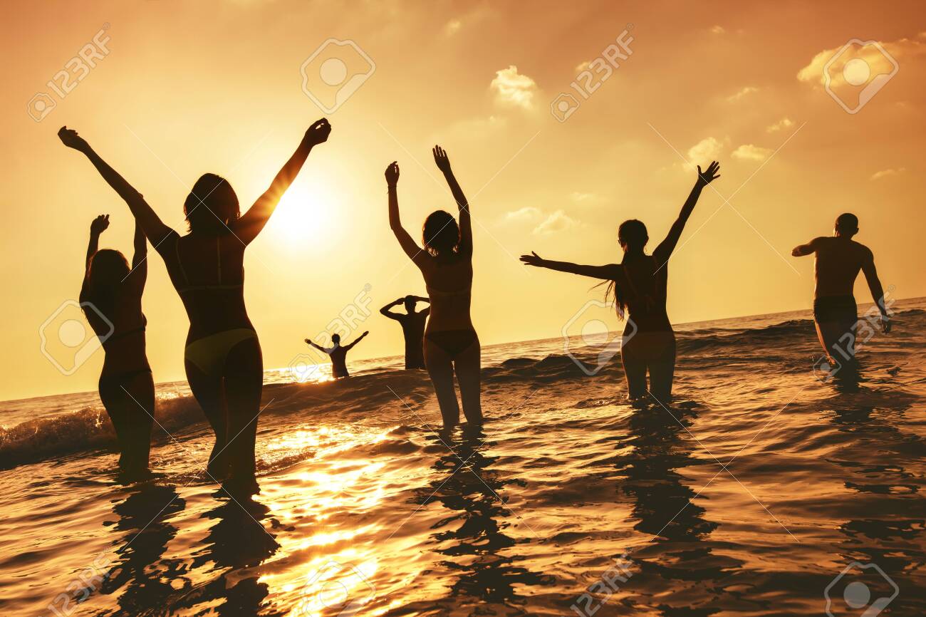 Big group of happy peoples stands at sunset sea beach. Silhouettes with raised arms - 140964025 Big group of happy peoples stands at sunset sea beach. Silhouettes with raised arms - 140964025