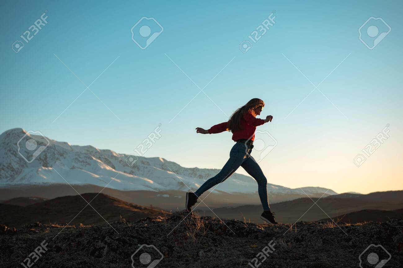 Slim sporty girl is walking in mountains at sunset time - 146896937 Slim sporty girl is walking in mountains at sunset time - 146896937