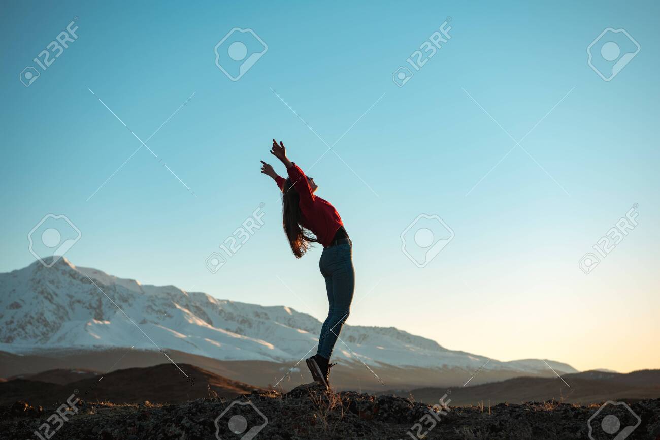 Young active girl is standing in winner pose in mountains at sunset or sunrise - 147026680 Young active girl is standing in winner pose in mountains at sunset or sunrise - 147026680