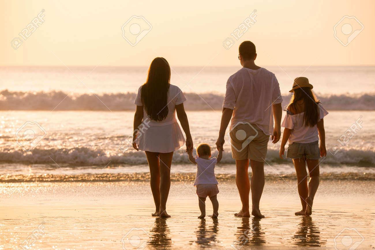 Family of four peoples in white are standing and relaxing at sunset sea beach - 155924900 Family of four peoples in white are standing and relaxing at sunset sea beach - 155924900