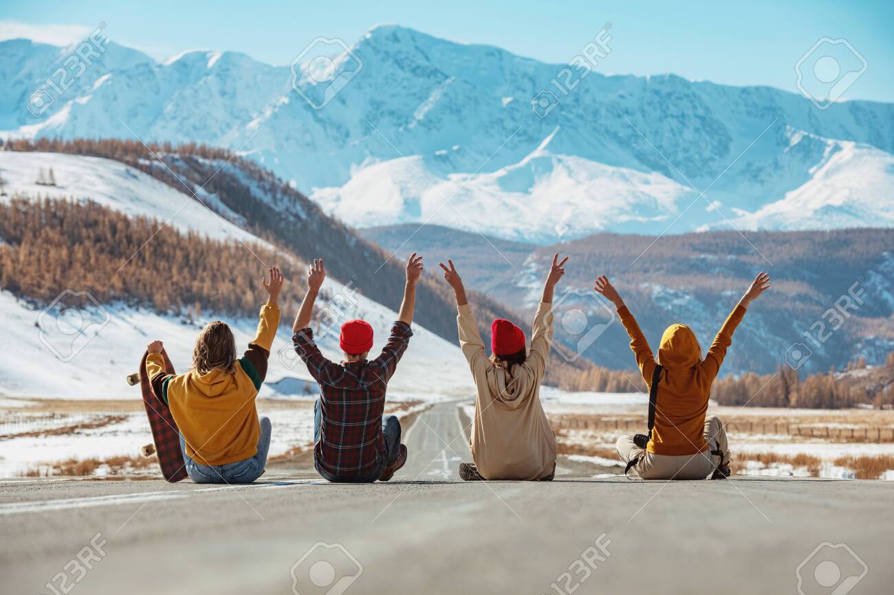 Four happy friends sits with raised arms on straight mountains road and having fun. Travel concept - 157598986 Four happy friends sits with raised arms on straight mountains road and having fun. Travel concept - 157598986