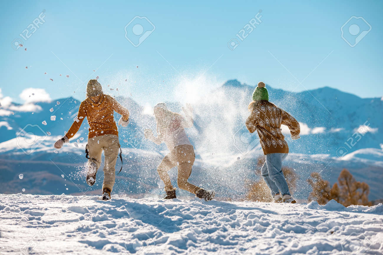 Three young happy girls friends are having fun in snow fight in mountains. First snow and winter vacations concept - 159063630 Three young happy girls friends are having fun in snow fight in mountains. First snow and winter vacations concept - 159063630