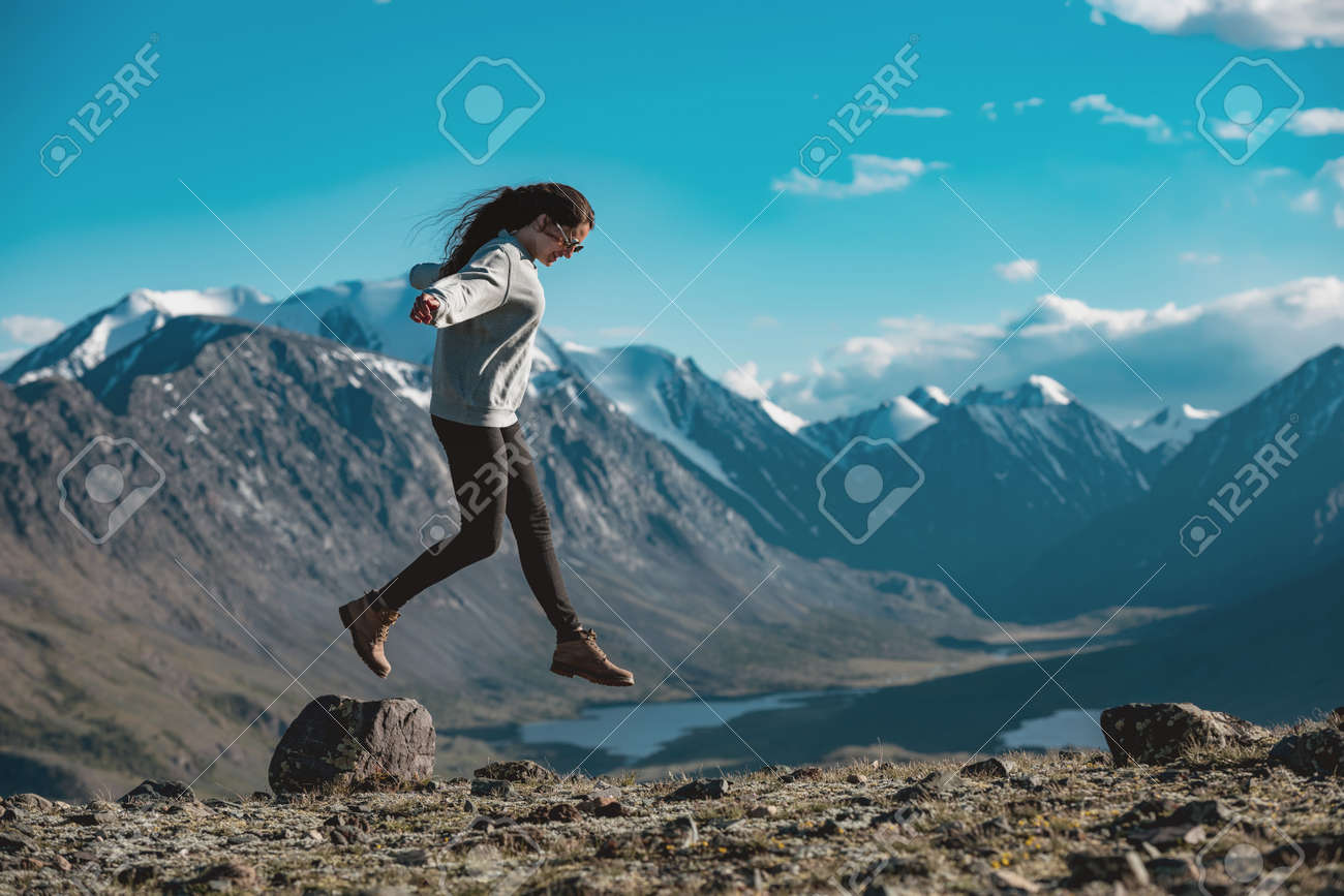 One slim sporty girl is having fun and jumps over the stone in high mountains. Active tourism concept - 159302212 One slim sporty girl is having fun and jumps over the stone in high mountains. Active tourism concept - 159302212