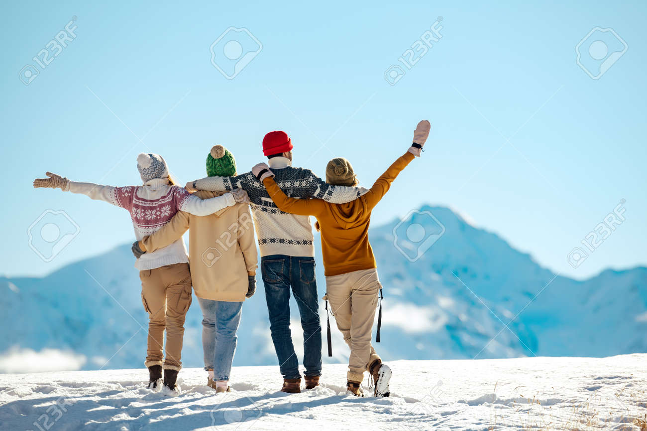 Four happy friends are standing and embracing against snow capped mountains at sunny day. Winter vacations concept - 159506361 Four happy friends are standing and embracing against snow capped mountains at sunny day. Winter vacations concept - 159506361