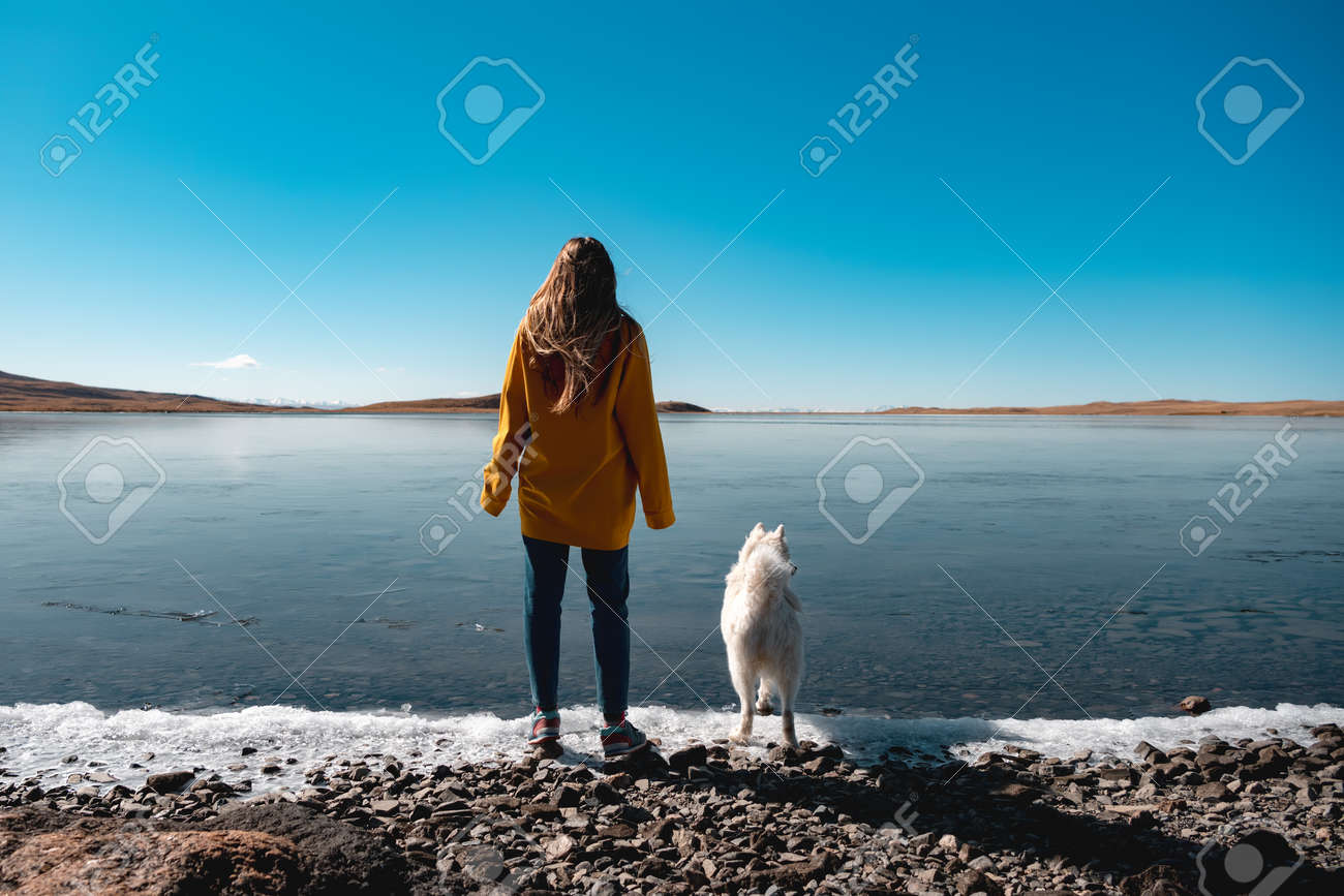 Young girl with white husky stands at frozen lake beach - 159900600 Young girl with white husky stands at frozen lake beach - 159900600