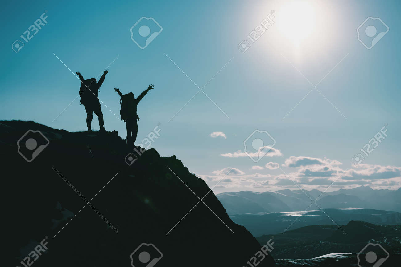 Silhouettes of two happy hikers in winner poses with raised arms are standing on mountain top - 163777781 Silhouettes of two happy hikers in winner poses with raised arms are standing on mountain top - 163777781
