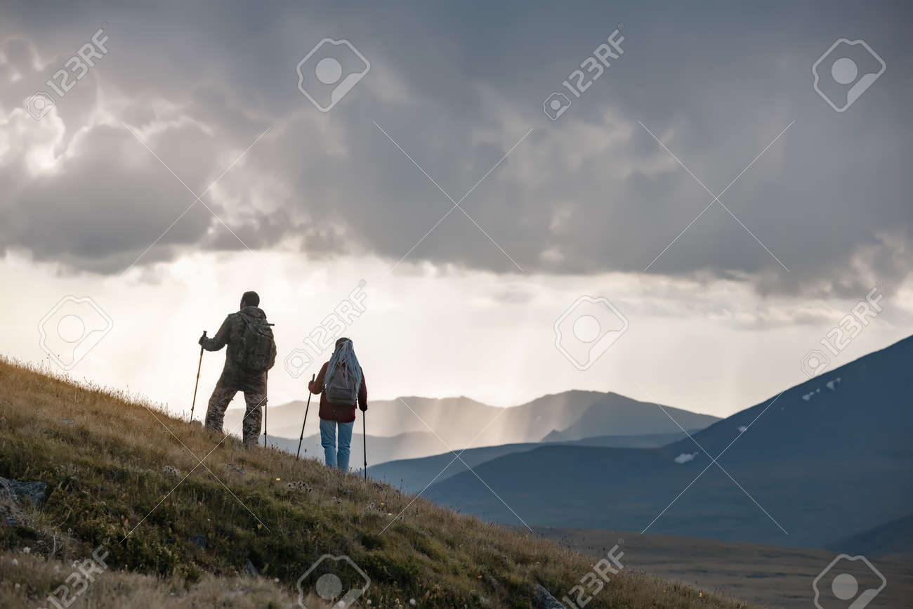Two young hikers are standing on mountain slope against sunset rainy sky - 163964985 Two young hikers are standing on mountain slope against sunset rainy sky - 163964985
