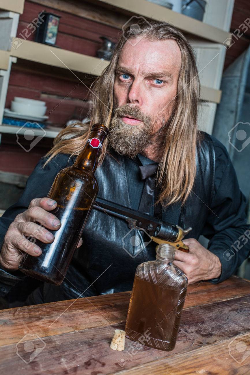 Drunk Man West Ziele Gun Gegen Flasche Während Er Am Tisch Sitzt
