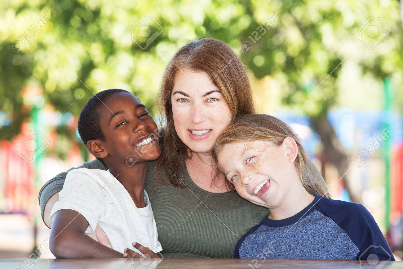 Joyful single parent sitting in between adopted child and son at table in park - 66190581 Joyful single parent sitting in between adopted child and son at table in park - 66190581