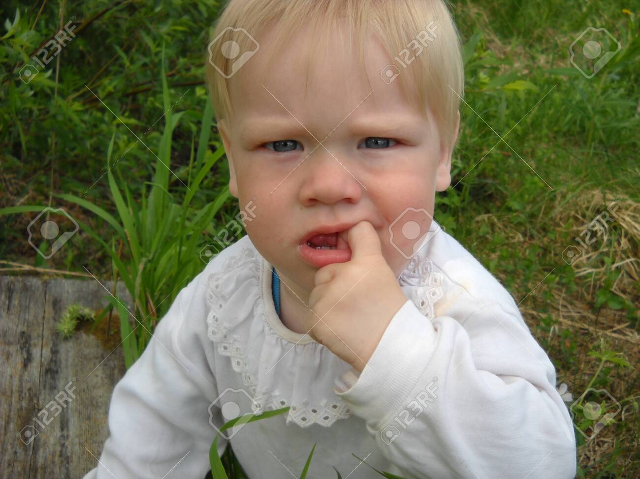 blonde hair boy mouth Petrozavodsk / Russia - July 01, 2019: A Small Child With Blond Hair Holds  A Finger In His Mouth. The Kid Is Wearing A White Shirt With A Frill. The  Boy Has
