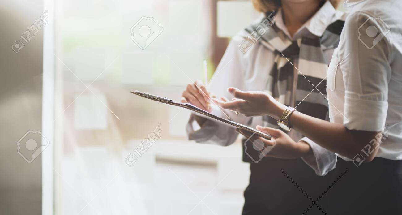 Young businesswomen discussing the company project together while holding tablet - 128394078 Young businesswomen discussing the company project together while holding tablet - 128394078