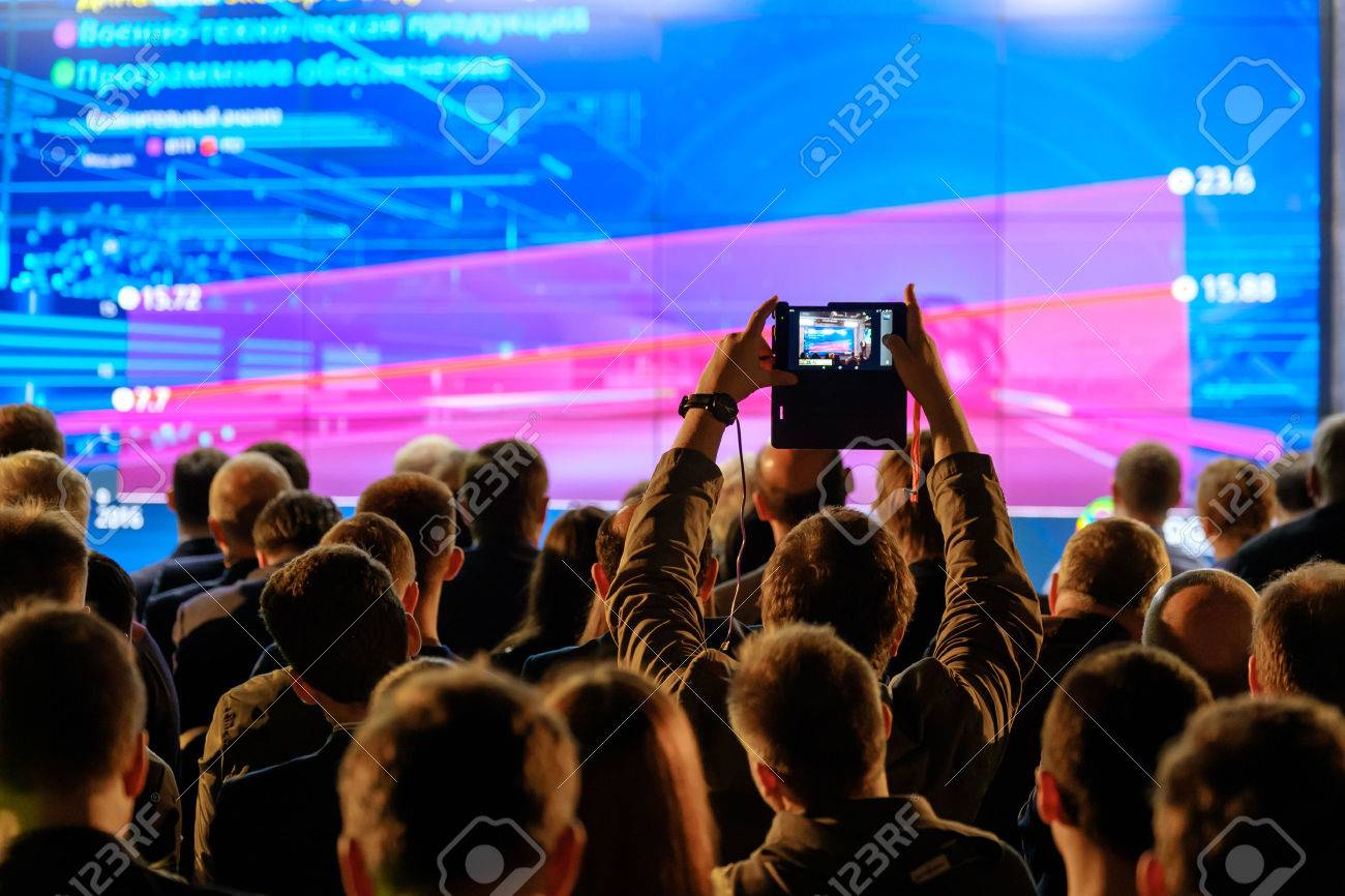 Man takes a picture of the presentation at the conference hall using smartphone - 78534199 Man takes a picture of the presentation at the conference hall using smartphone - 78534199
