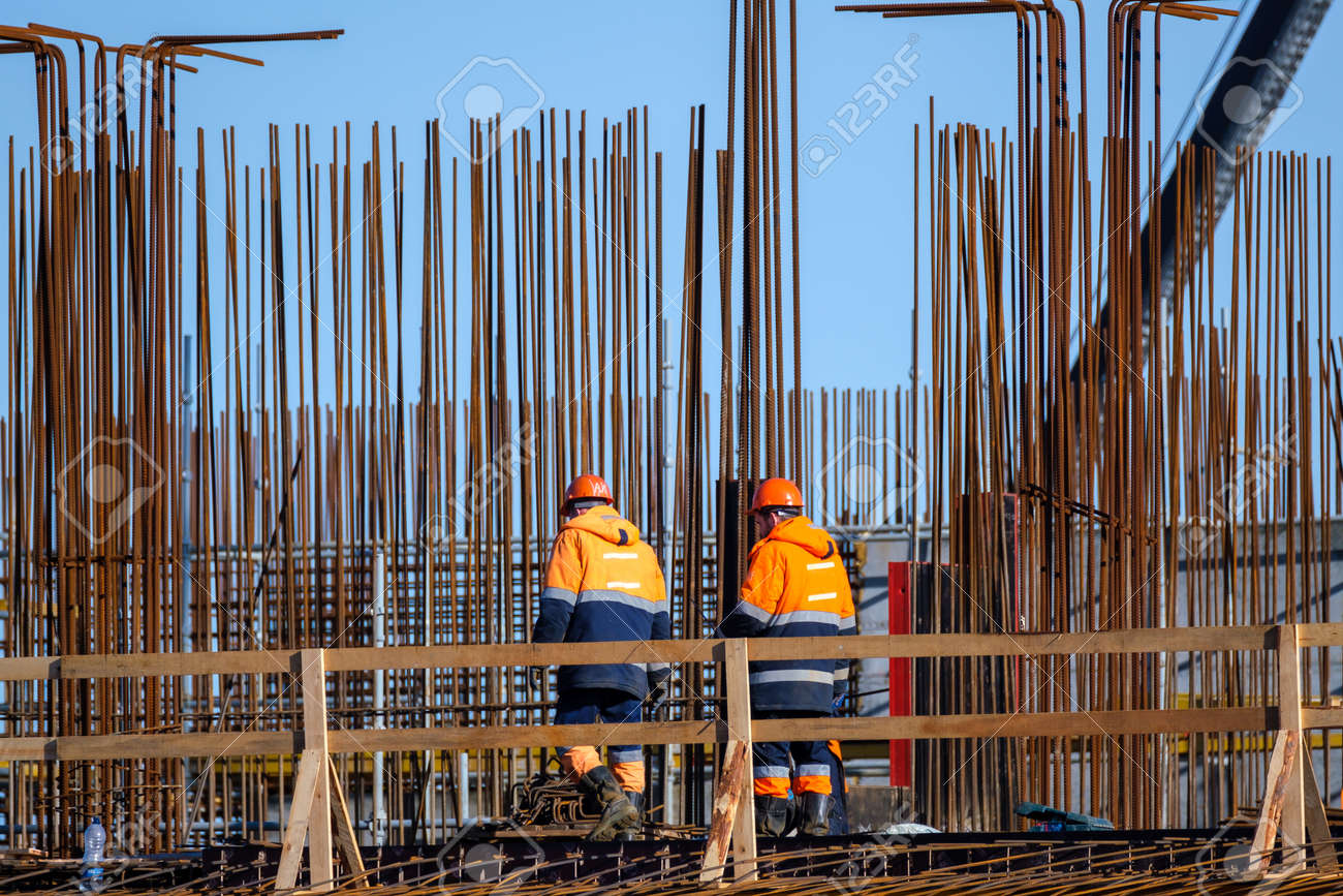 Back view of anonymous men in uniform walking near wooden railing and metal poles during work on construction site - 166802183 Back view of anonymous men in uniform walking near wooden railing and metal poles during work on construction site - 166802183