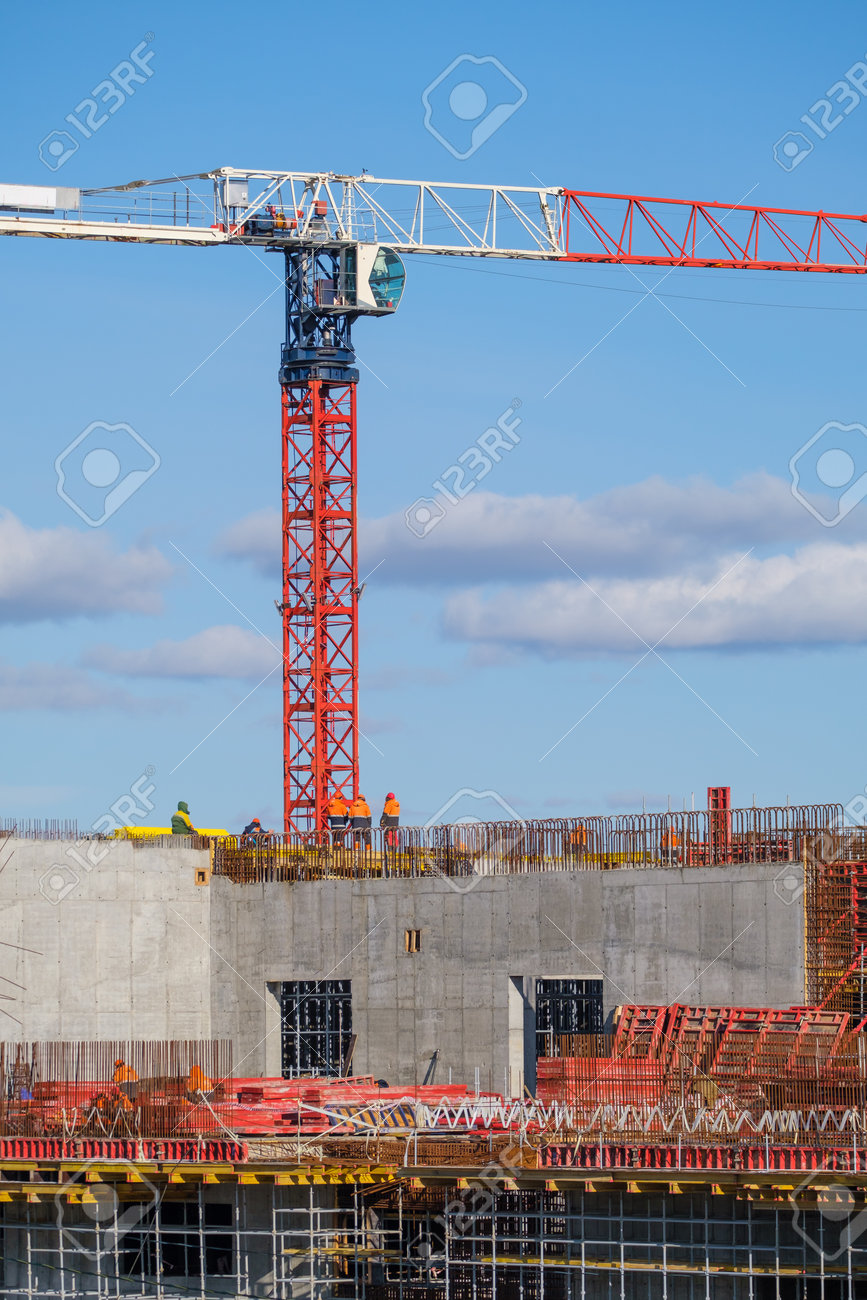 Tall crane located near unfinished building walls with builders against cloudy blue sky on construction site - 166806247 Tall crane located near unfinished building walls with builders against cloudy blue sky on construction site - 166806247