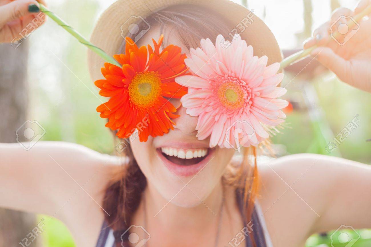 Young woman covering her eyes with fresh colorful flowers. Enjoying..