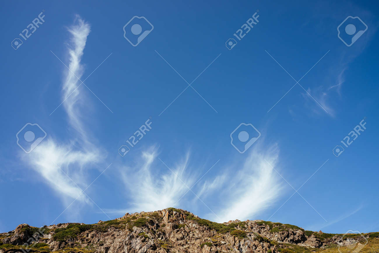 Scenic mountain landscape with beautiful cirrus clouds in clear blue sky over rocks in sunlight. Colorful highland scenery with spindrift clouds in blue clear sky above green brown rocky mountains. - 170160614 Scenic mountain landscape with beautiful cirrus clouds in clear blue sky over rocks in sunlight. Colorful highland scenery with spindrift clouds in blue clear sky above green brown rocky mountains. - 170160614