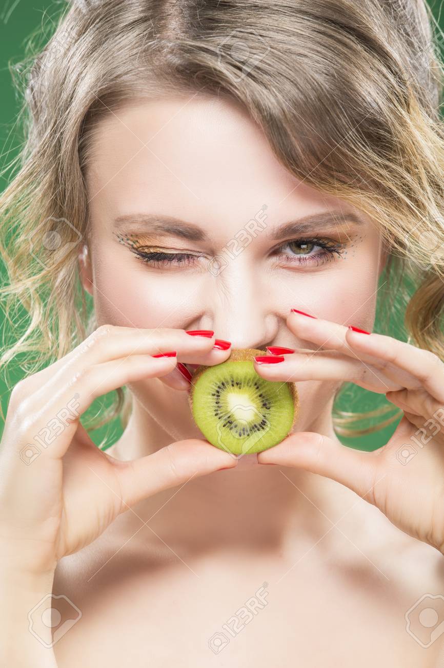 フルーツ キウイ シリーズのアイデア ジューシーなキウイ フルーツの口の前でポーズをとって歯間離開と裸の白人モデルの まばたき の 肖像画 に対してグリーン 垂直方向の画像の合成 の写真素材 画像素材 Image