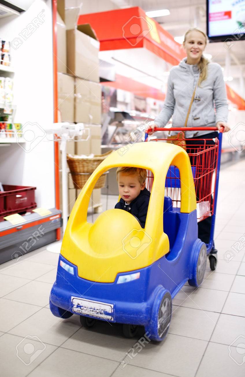 Enfants Courses Au Supermarche Avec Une Jeune Mere Poussant Son Petit Fils Dans Une Voiture En Plastique Colore Attache Au Chariot Lui Garder Heureux Et De Se Divertir Tout En Elle Achete