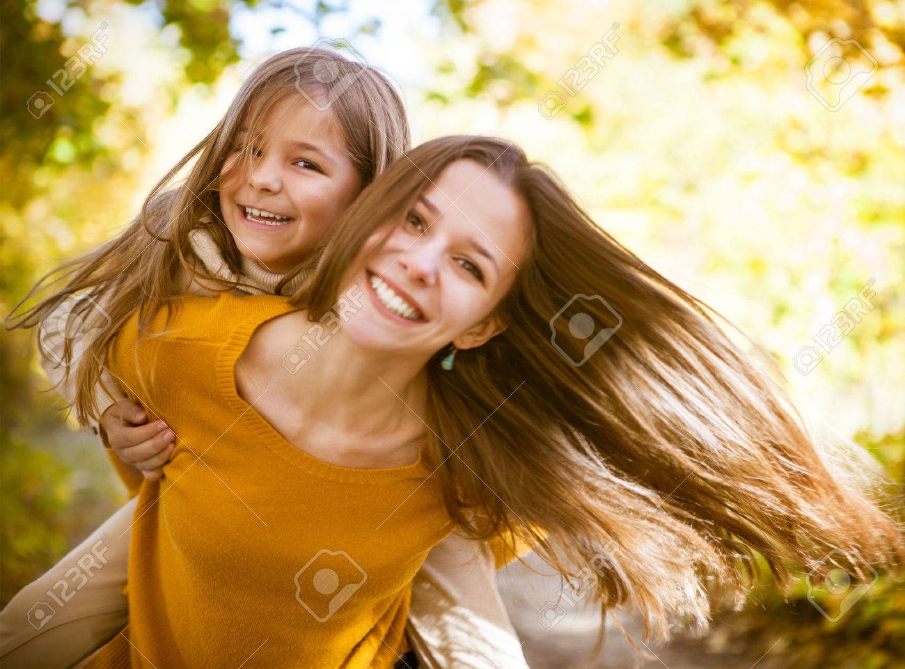 Two cheerful sisters playing in the park in warm autumn day - 44363268 Two cheerful sisters playing in the park in warm autumn day - 44363268