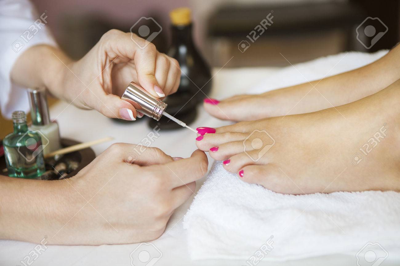 Woman in nail salon receiving pedicure by beautician. Close up of female feet resting on white towel - 48002403 Woman in nail salon receiving pedicure by beautician. Close up of female feet resting on white towel - 48002403