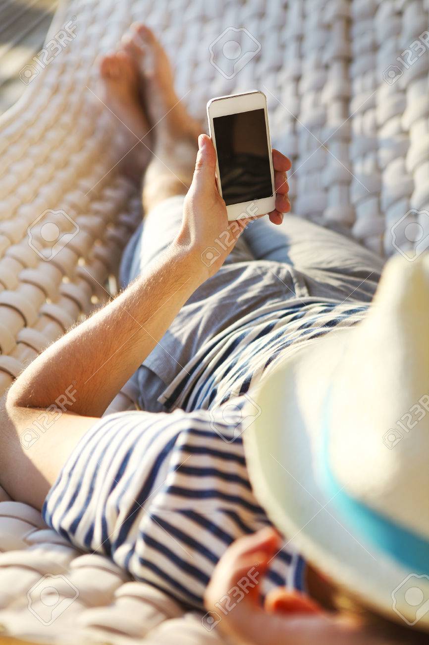 Lazy time. Man in hat in a hammock with mobile phone on a summer day - 50767185 Lazy time. Man in hat in a hammock with mobile phone on a summer day - 50767185
