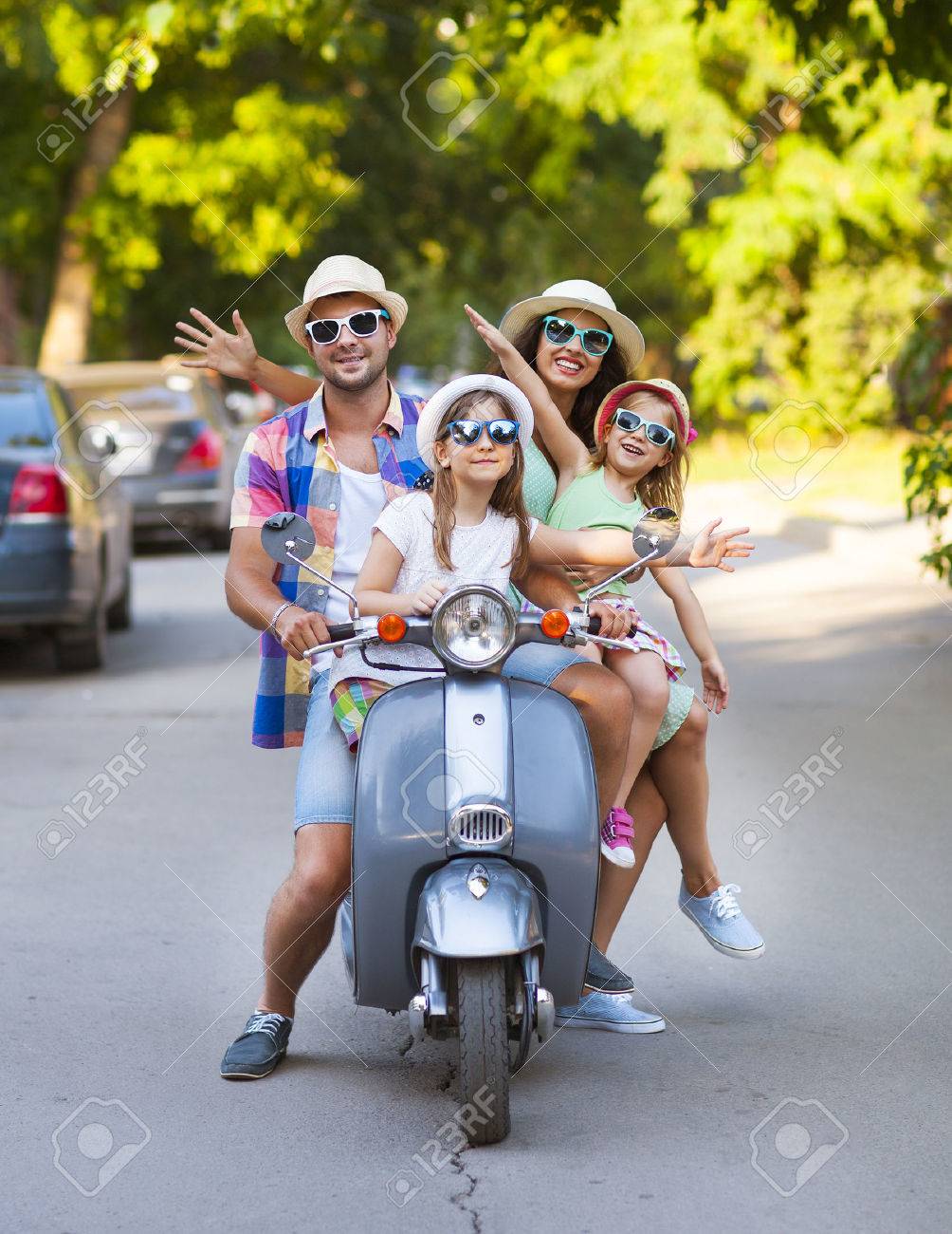 Happy young family riding a vintage scooter in the street wearing hats and sunglasses. Holiday and travel concept - 50955919 Happy young family riding a vintage scooter in the street wearing hats and sunglasses. Holiday and travel concept - 50955919