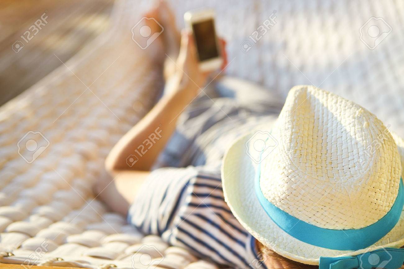 Lazy time. Man in hat in a hammock with mobile phone on a summer day - 51550215 Lazy time. Man in hat in a hammock with mobile phone on a summer day - 51550215