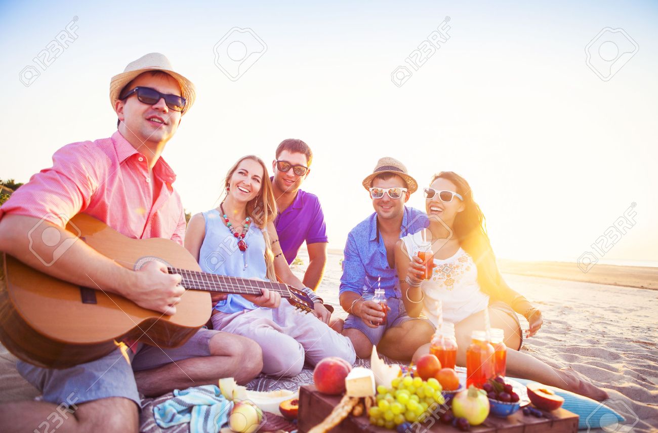 Friends sitting on the sand at the beach in circle. One man is playing guitar - 52963671 Friends sitting on the sand at the beach in circle. One man is playing guitar - 52963671