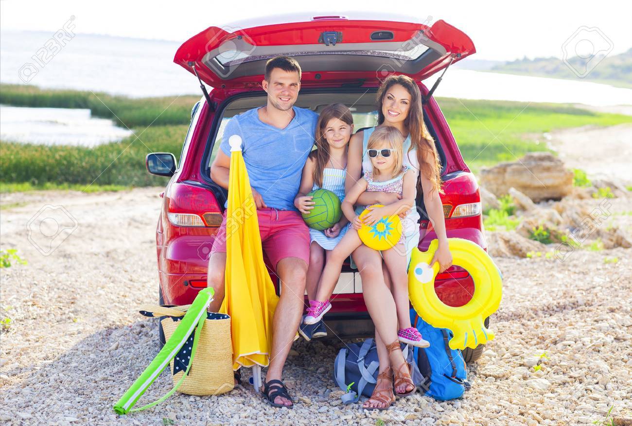 Portrait of a smiling family with two children at beach by car. Holiday and travel concept - 57290516 Portrait of a smiling family with two children at beach by car. Holiday and travel concept - 57290516