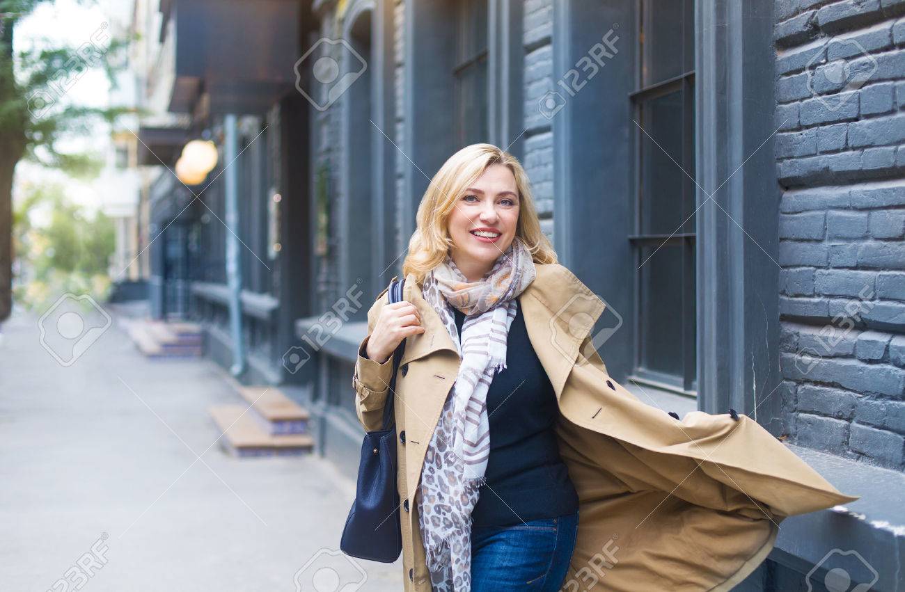 Middle age woman goes through the city and smiles. Happiness concept. - 70536455 Middle age woman goes through the city and smiles. Happiness concept. - 70536455