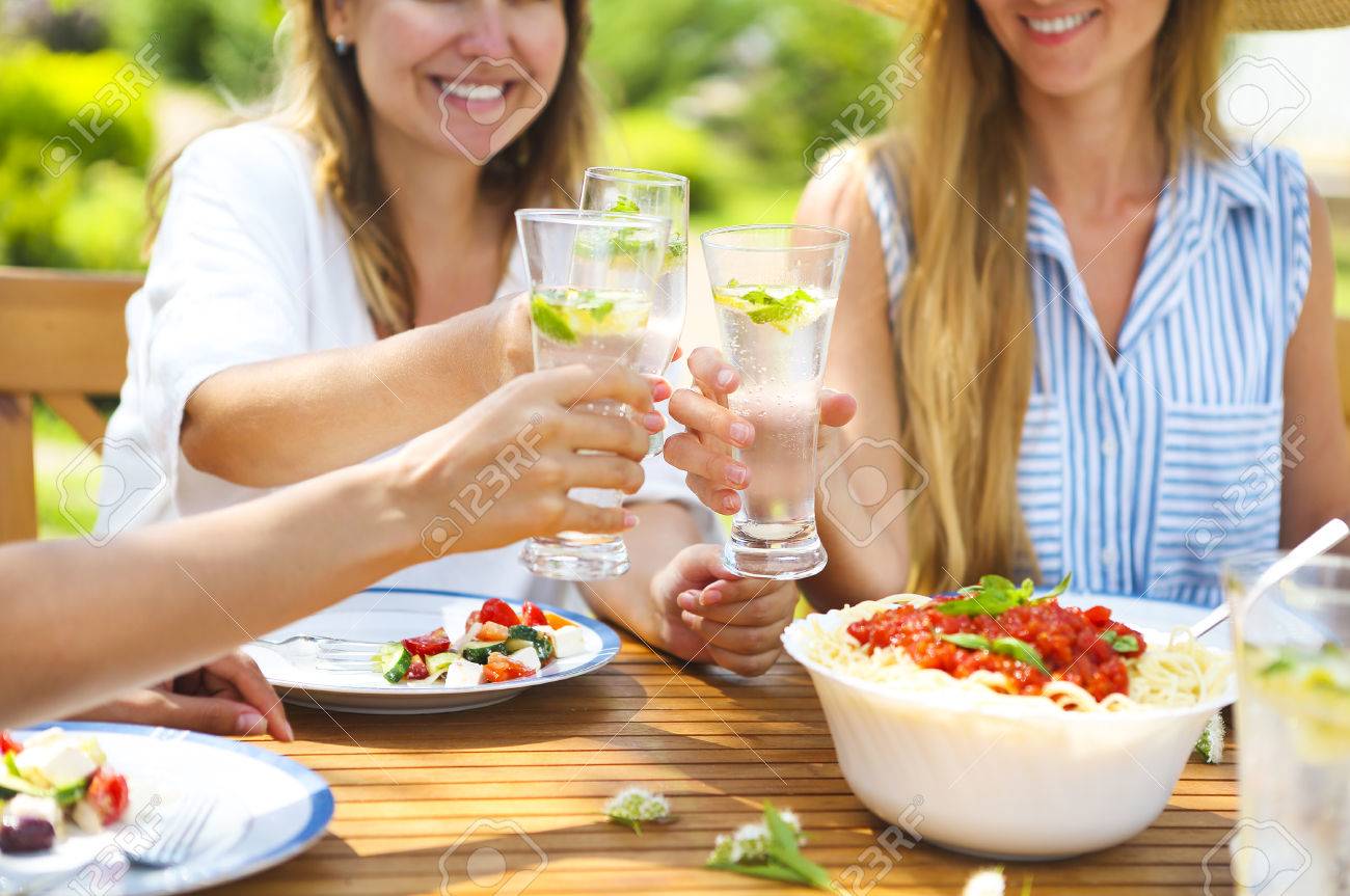 Happy female friends with glasses of lemonade at dining table in lawn. Close up - 78820000 Happy female friends with glasses of lemonade at dining table in lawn. Close up - 78820000