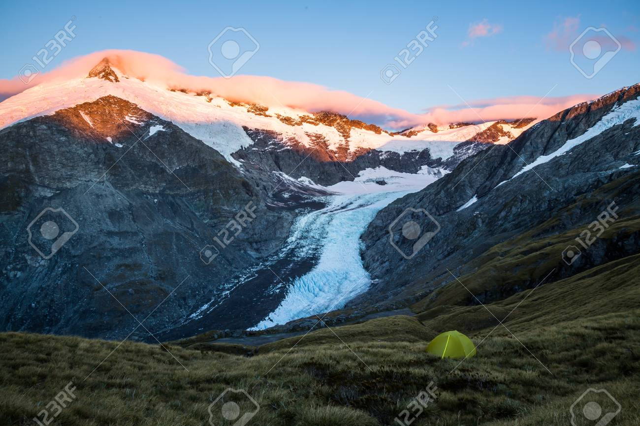 A Beautiful Camping Site With A Backdrop Of Tall Alpine Peaks Covered In Glaciers Below A Beautiful Camping Site With A Backdrop Of Tall Alpine Peaks Covered In Glaciers Below