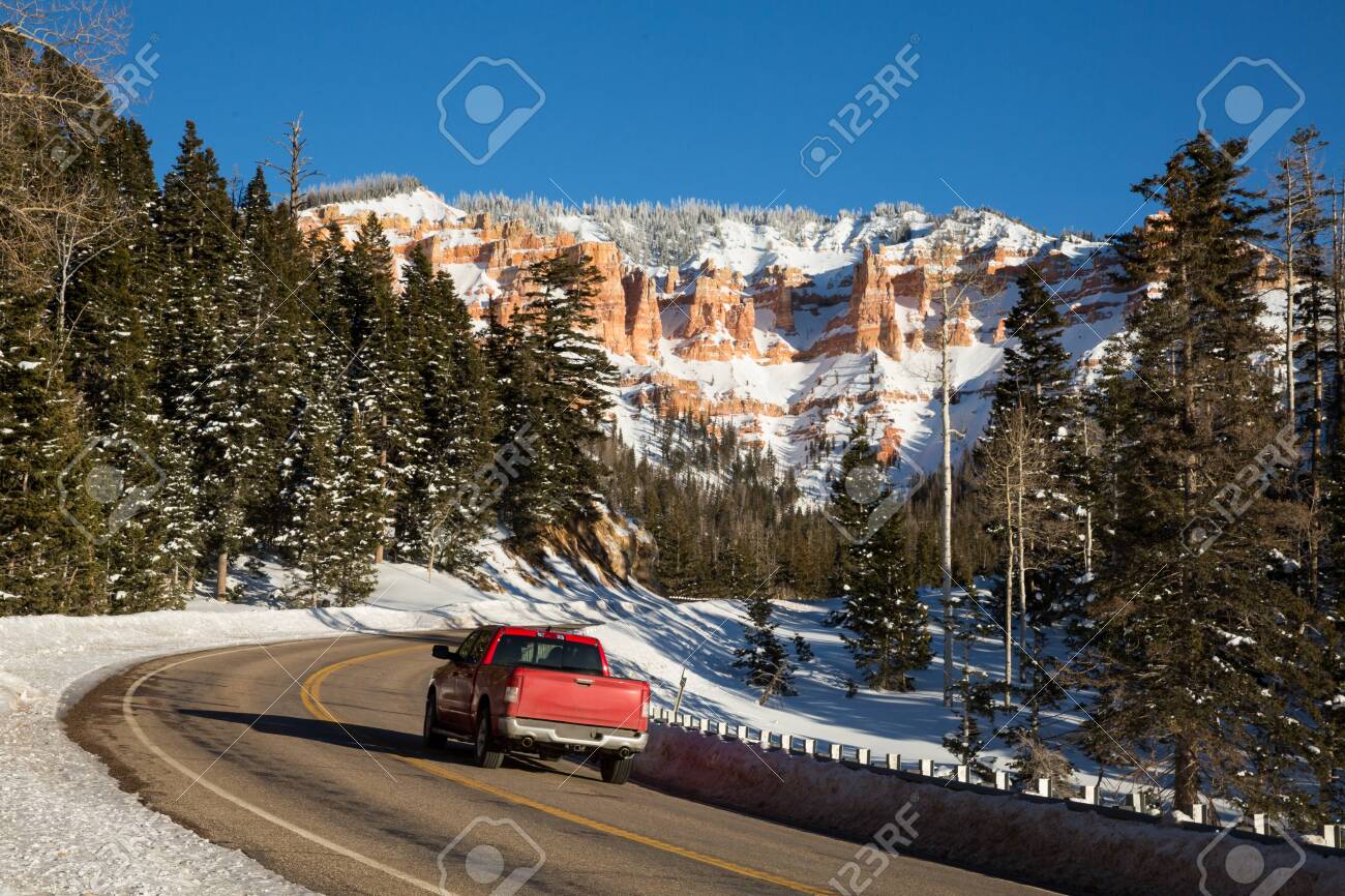 Red pickup driving up a winding canyon road toward snow covered rock formations in the red and orange sandstone. - 144644309 Red pickup driving up a winding canyon road toward snow covered rock formations in the red and orange sandstone. - 144644309