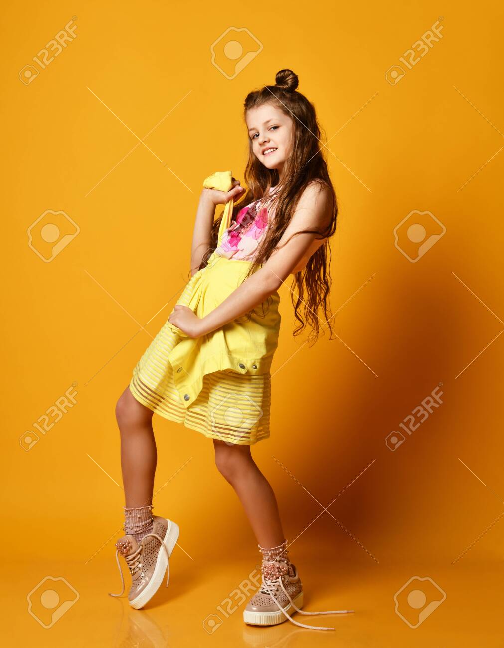 little tten Full Length Portrait Of A Cute Little Teen Girl In Stylish Skirt And Jacket  Clothing Knotted At The Waist, Looking At The Camera And Smiling Against A  Yellow Studio Wall. Children's Fashion