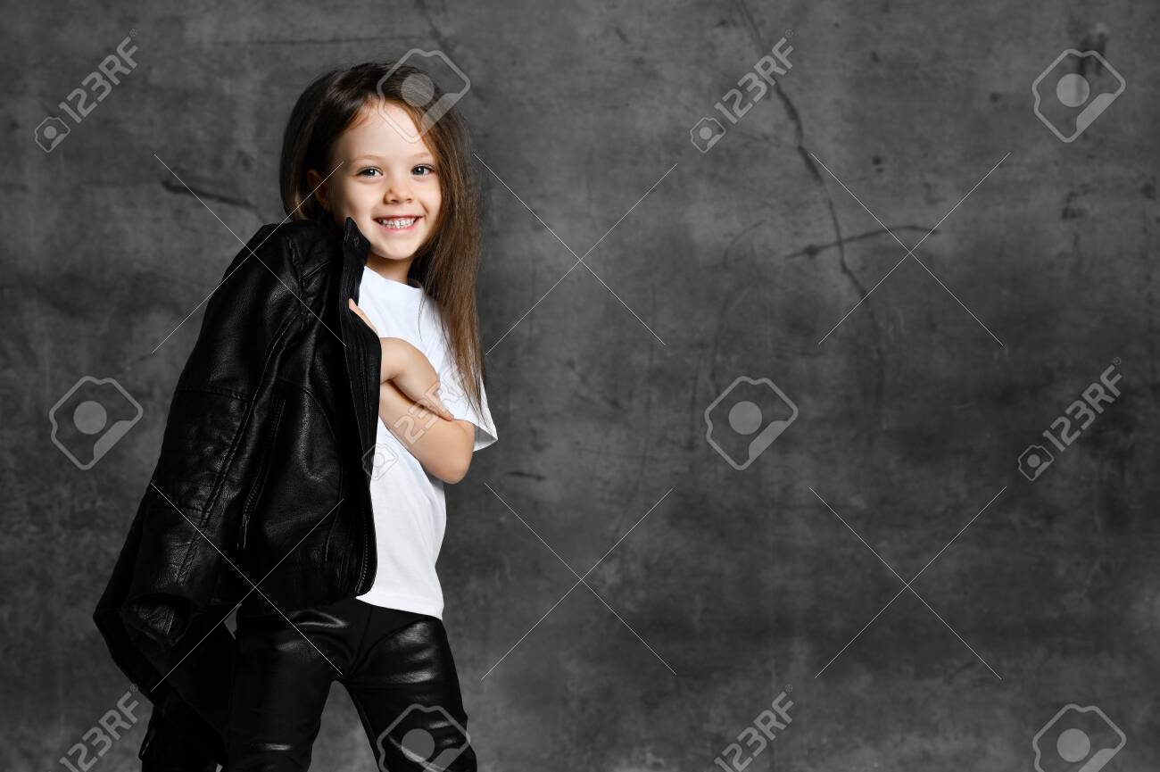 Small smiling cute girl in black and white rock star style casual clothing and white sneakers standing over grey concrete background in photo studio. Stylish children clothing concept - 136436565 Small smiling cute girl in black and white rock star style casual clothing and white sneakers standing over grey concrete background in photo studio. Stylish children clothing concept - 136436565