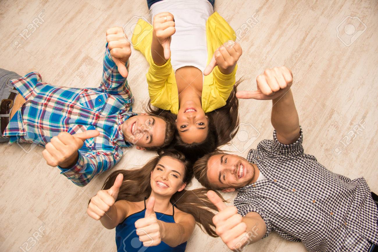Cheerful Young People Lying On The Floor Showing Thumbs Up Stock