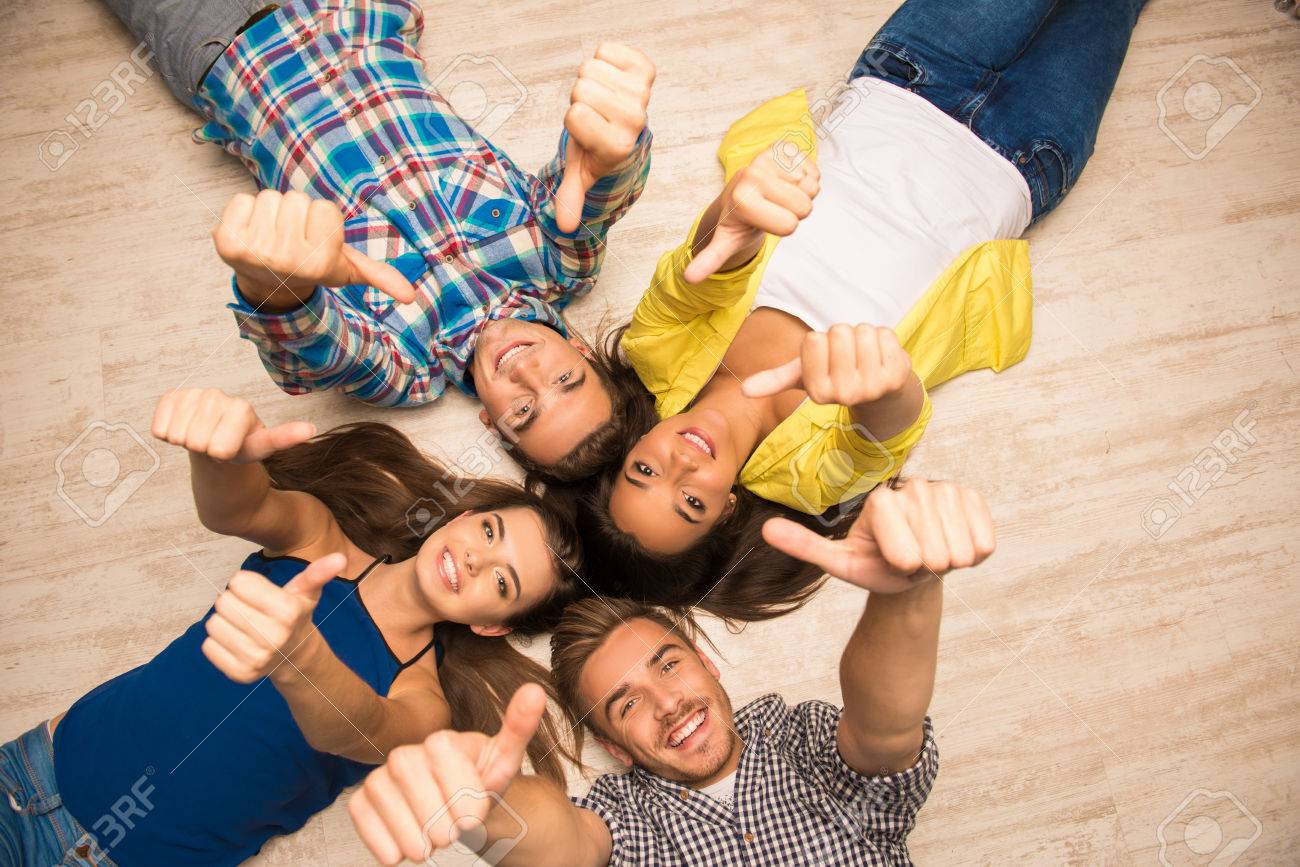 Cheerful Young People Lying On The Floor Showing Thumbs Up Stock