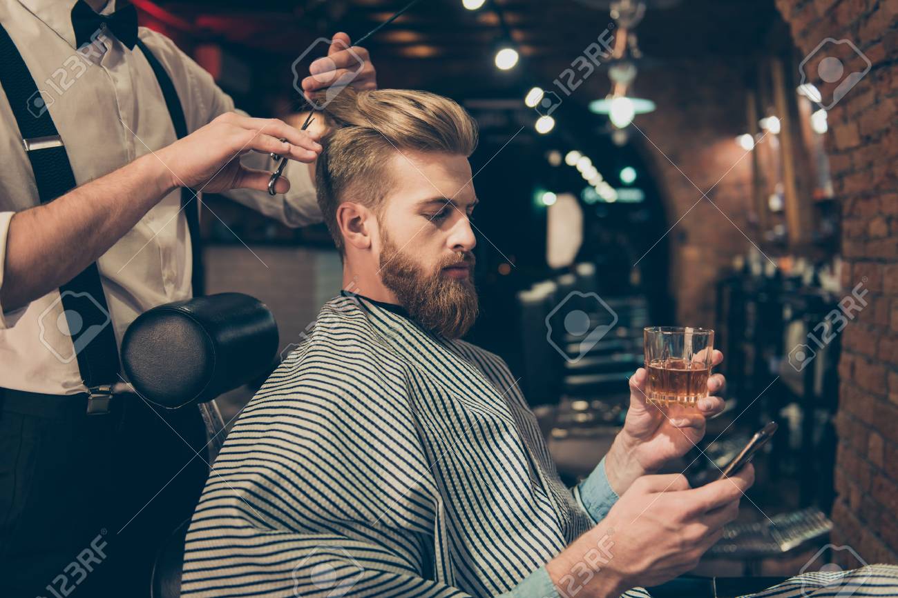 Chill out at the barber shop. Side view of handsome young red bearded man drinking scotch and browsing at his pda, while getting a haircut - 82694152 Chill out at the barber shop. Side view of handsome young red bearded man drinking scotch and browsing at his pda, while getting a haircut - 82694152