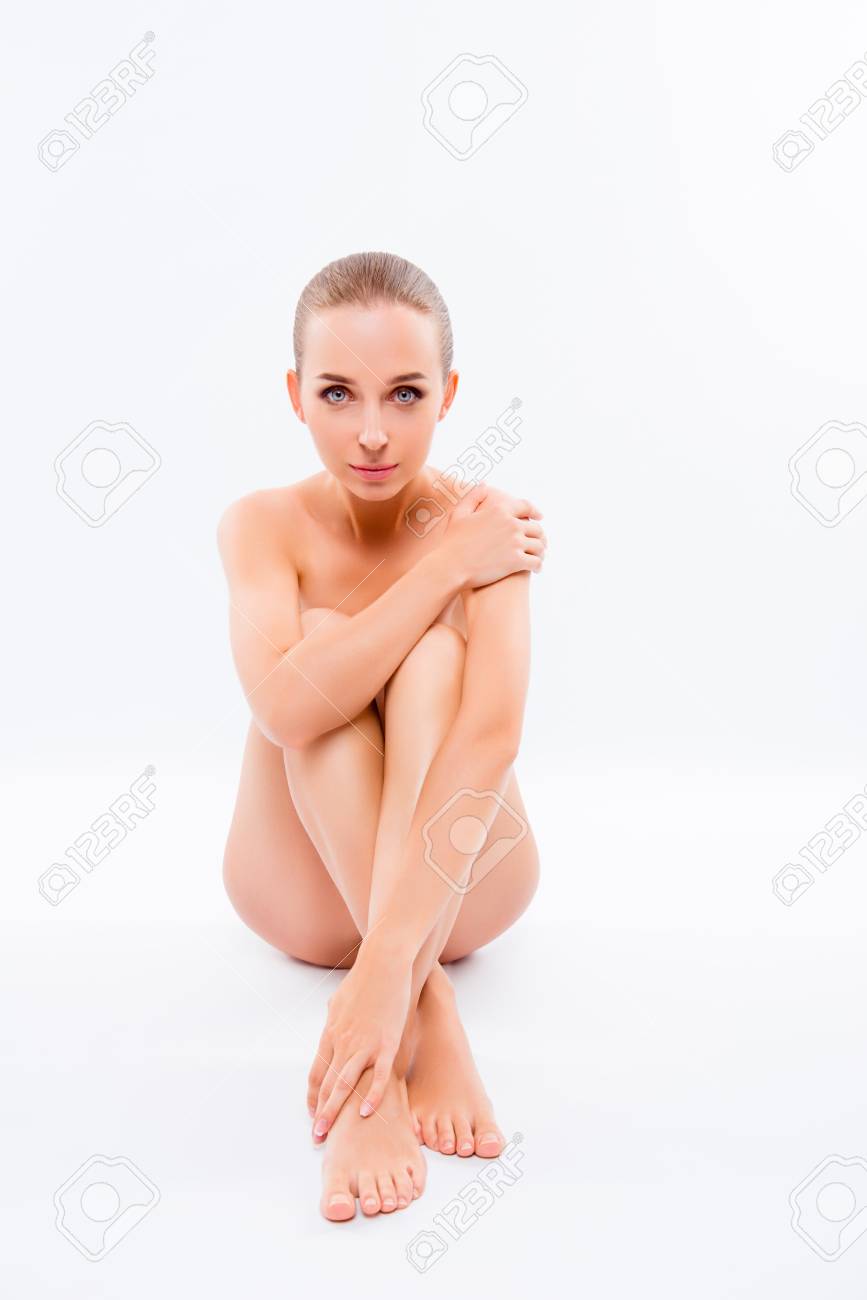 Vertical Retrato De Mujer Joven Sin Ropa Interior Está Sentada En El Suelo Y Cubriendo Su Impecable Cuerpo Limpio Y Liso Con Las Manos, Aislado Fondo Blanco. Fotos, Retratos, Imágenes