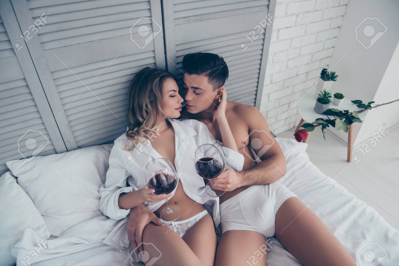 Hermosa Pareja Abrazándose Acostada En La Cama Con Copas De Vino Medio  Desnudas En Un Atuendo Sexy Blanco, Disfrutando, Placer, Besando, Toque  Suave, Fin De Semana, Festivo, Celebrando San Valentín, 14 De