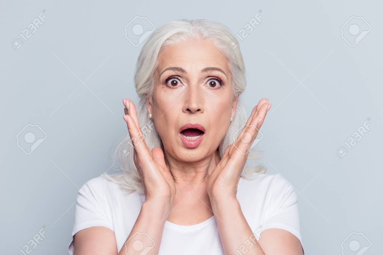 Pretty, nice, old, shocked, scared woman with wide open eyes and mouth in t-shirt holding palms near cheeks looking at camera over gray background - 95427481 Pretty, nice, old, shocked, scared woman with wide open eyes and mouth in t-shirt holding palms near cheeks looking at camera over gray background - 95427481
