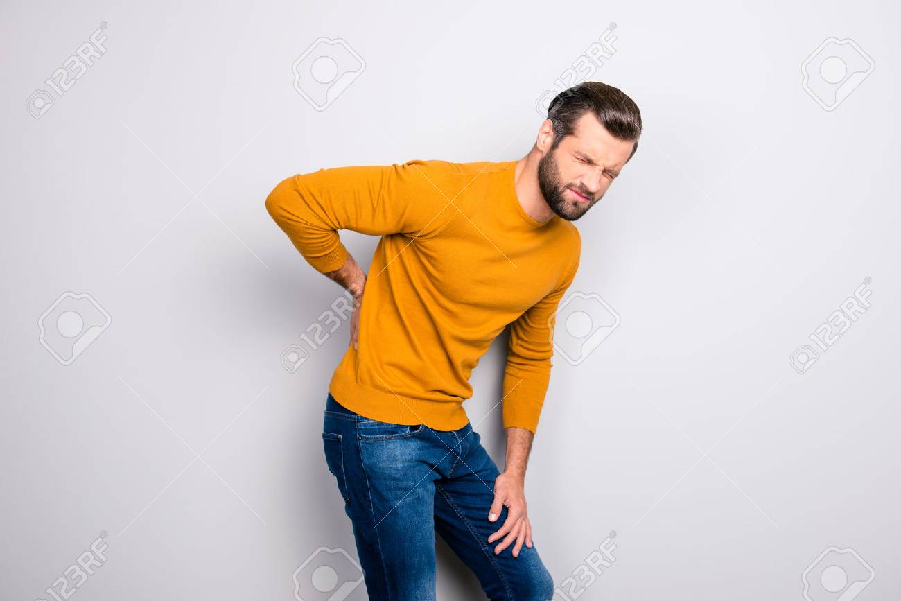 Side profile half-turned portrait of grimacing sad upset unhappy with serious pain in back man wearing yellow tight sweater and jeans isolated on gray background copy-space - 105714036 Side profile half-turned portrait of grimacing sad upset unhappy with serious pain in back man wearing yellow tight sweater and jeans isolated on gray background copy-space - 105714036