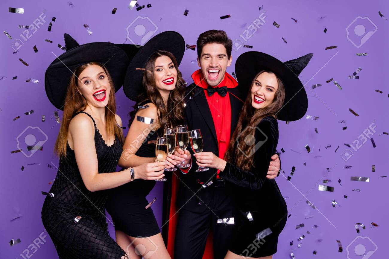 Photo of witch ladies and wizard guy at helloween event drink golden wine glitter flying in air wear black dresses caps suit and long coat isolated purple color background - 130343381 Photo of witch ladies and wizard guy at helloween event drink golden wine glitter flying in air wear black dresses caps suit and long coat isolated purple color background - 130343381