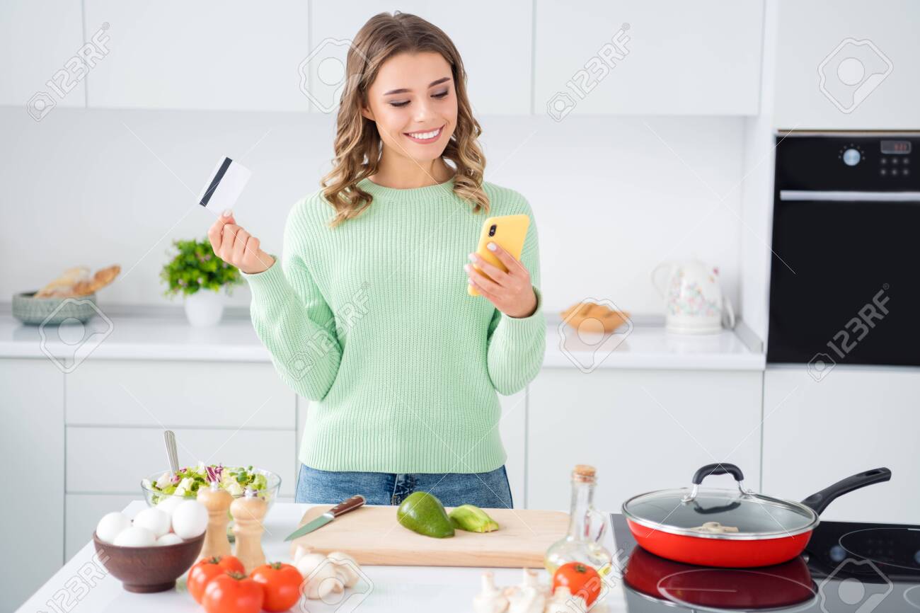 Portrait of her she nice attractive lovely cheerful girl cooking fresh tasty yummy meal holding in hands ell bank card ordering vegs farm organic products in modern light white kitchen house - 149120932 Portrait of her she nice attractive lovely cheerful girl cooking fresh tasty yummy meal holding in hands ell bank card ordering vegs farm organic products in modern light white kitchen house - 149120932